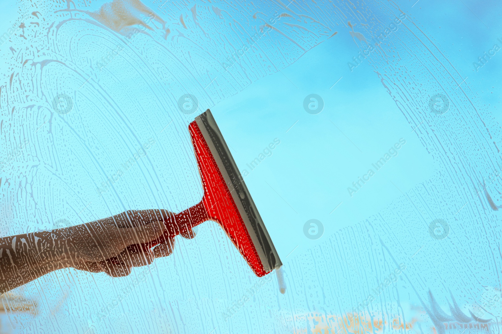 Photo of Woman cleaning window with squeegee on spring day, closeup