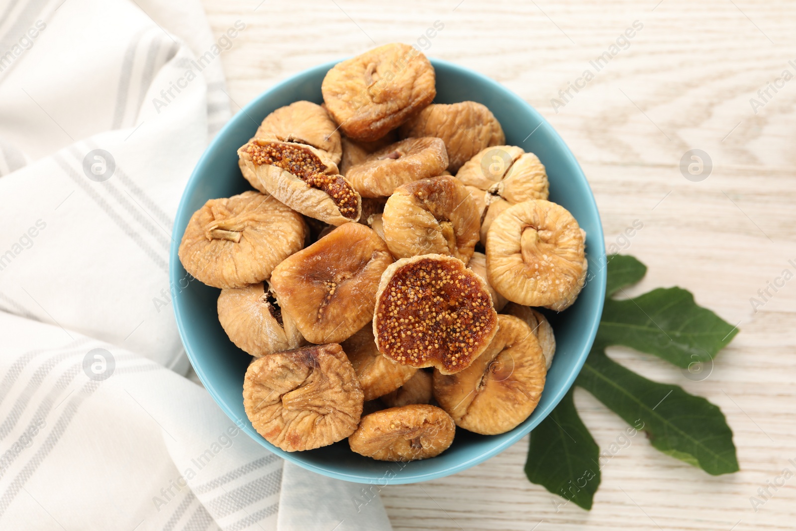 Photo of Bowl with tasty dried figs and green leaf on white wooden table, top view