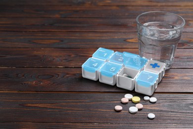 Photo of Pill box with medicaments and glass of water on wooden table. Space for text