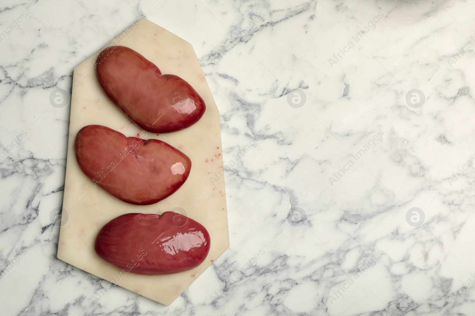 Photo of Fresh raw pork kidneys on white marble table, top view. Space for text