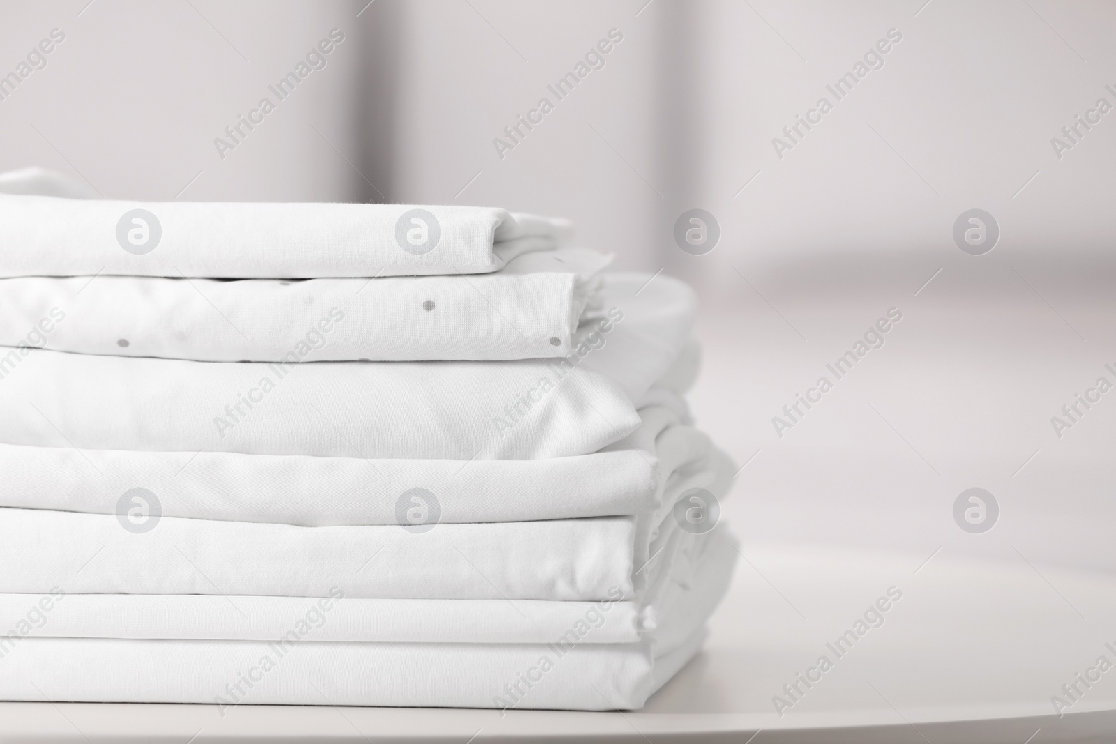 Photo of New clean folded bed linens on table indoors. Space for text