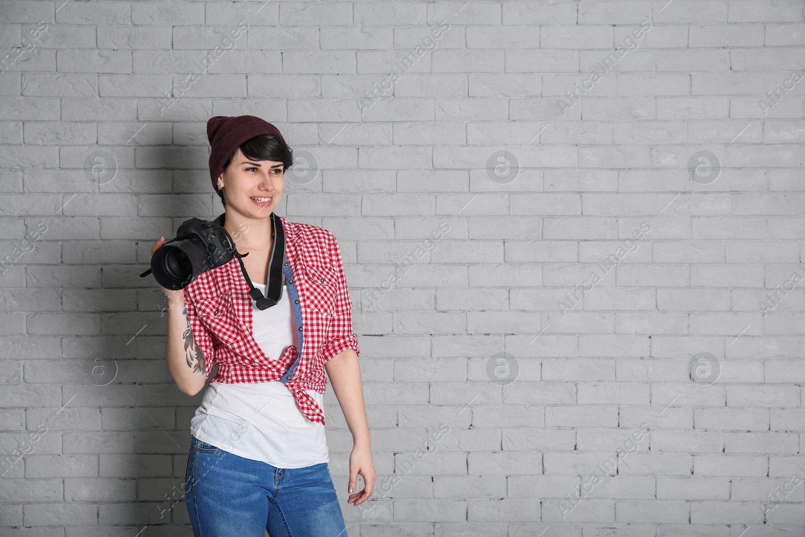 Photo of Young female photographer with camera on brick background