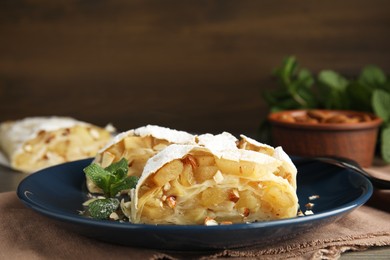 Photo of Delicious apple strudel with almonds, powdered sugar and mint on table, closeup. Space for text