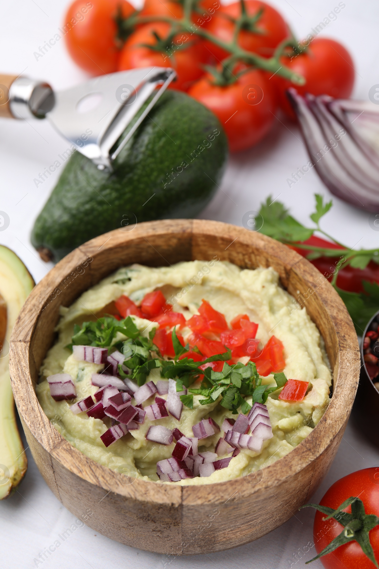 Photo of Bowl of delicious guacamole with onion, tomatoes and ingredients on white table