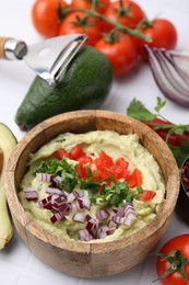 Bowl of delicious guacamole with onion, tomatoes and ingredients on white table