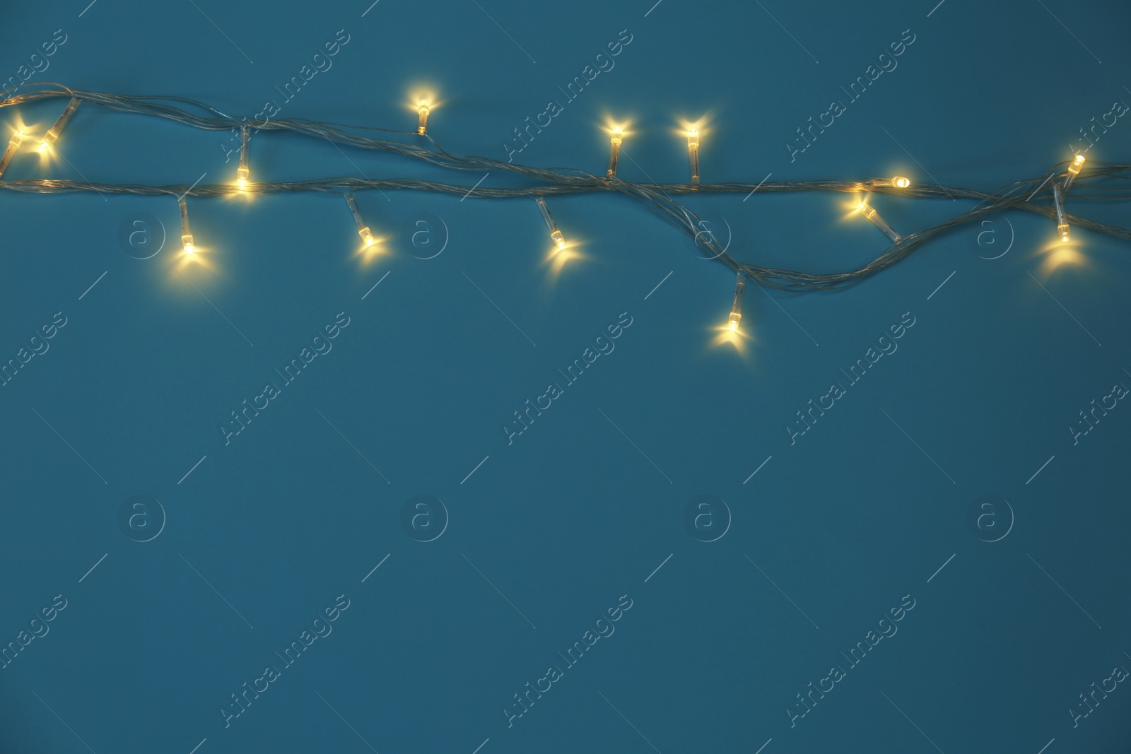 Photo of Glowing Christmas lights on blue background, top view. Space for text