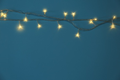 Photo of Glowing Christmas lights on blue background, top view. Space for text