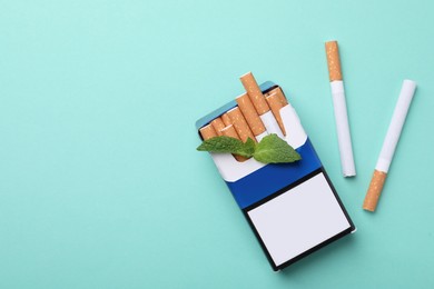 Photo of Pack of menthol cigarettes and mint on turquoise background, flat lay. Space for text