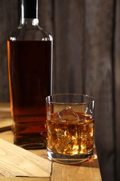 Photo of Whiskey with ice cubes in glass and bottle on wooden crate, closeup