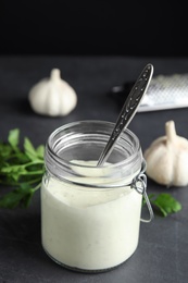 Photo of Jar of garlic sauce with spoon on kitchen table. Space for text