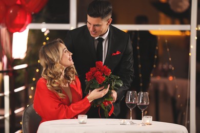 Photo of Man presenting roses to his beloved woman in restaurant at Valentine's day dinner