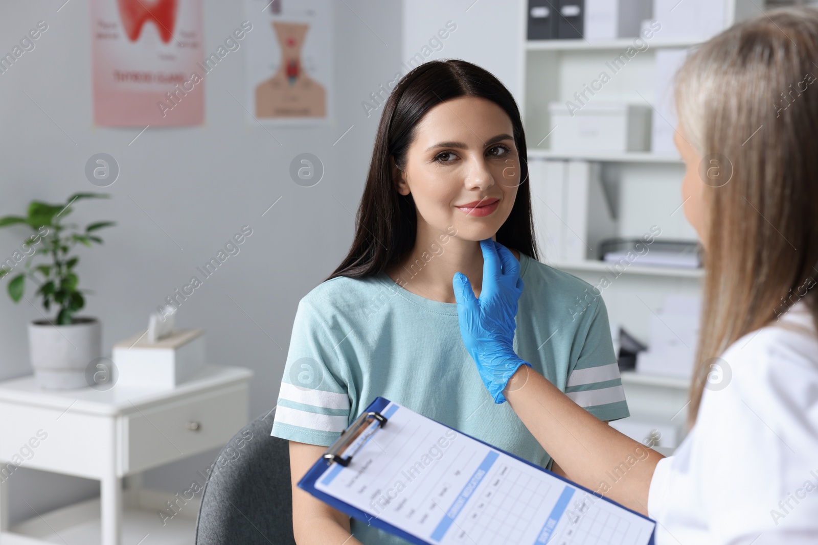 Photo of Endocrinologist with clipboard examining thyroid gland of patient at hospital