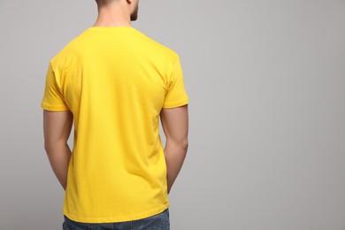 Photo of Man wearing yellow t-shirt on light grey background, back view. Mockup for design