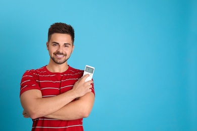 Photo of Happy young man with air conditioner remote control on light blue background. Space for text