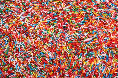 Photo of Bright colorful sprinkles as background, top view. Confectionery decor