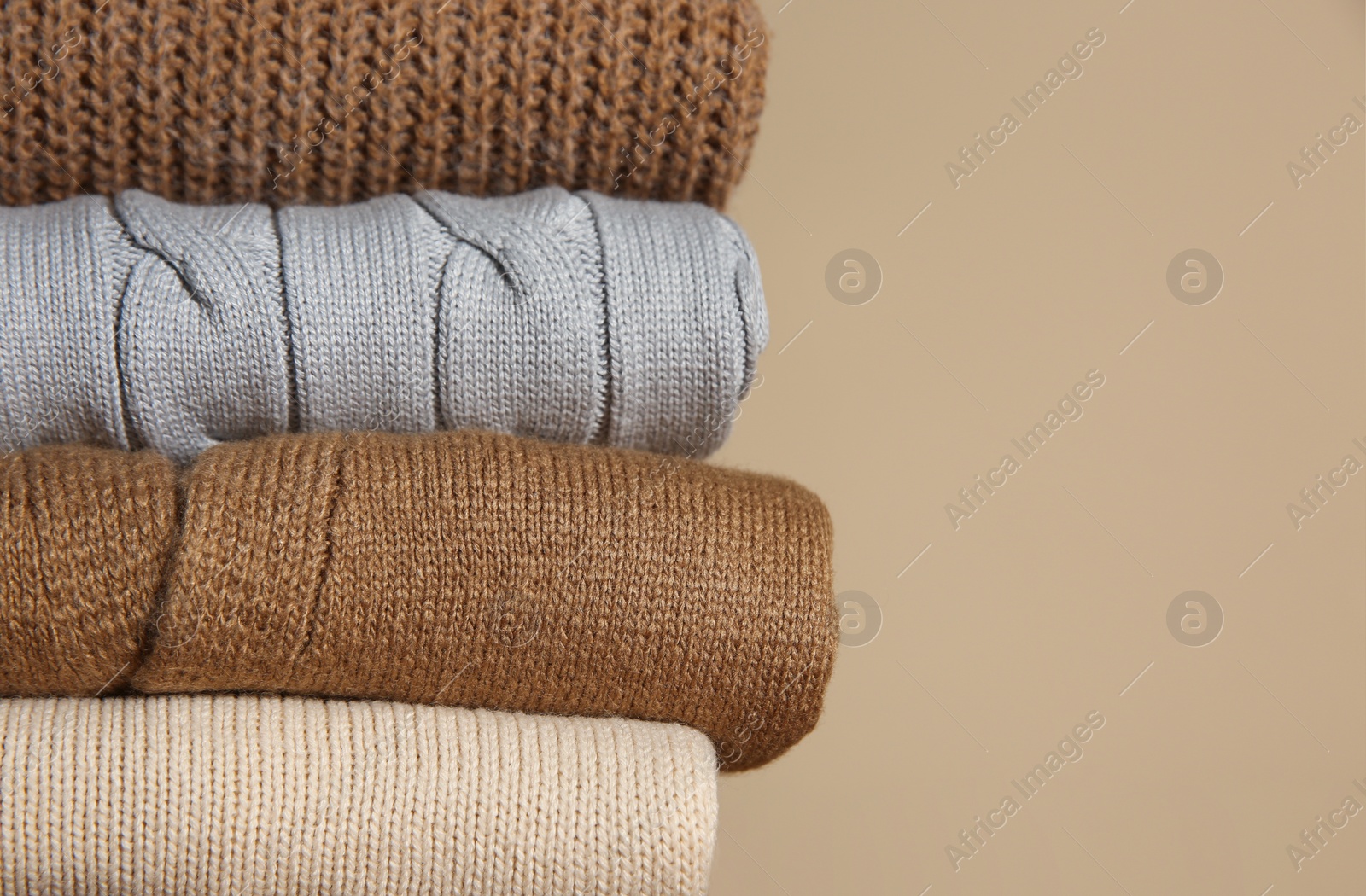 Photo of Stack of folded knitted sweaters on beige background, closeup. Space for text