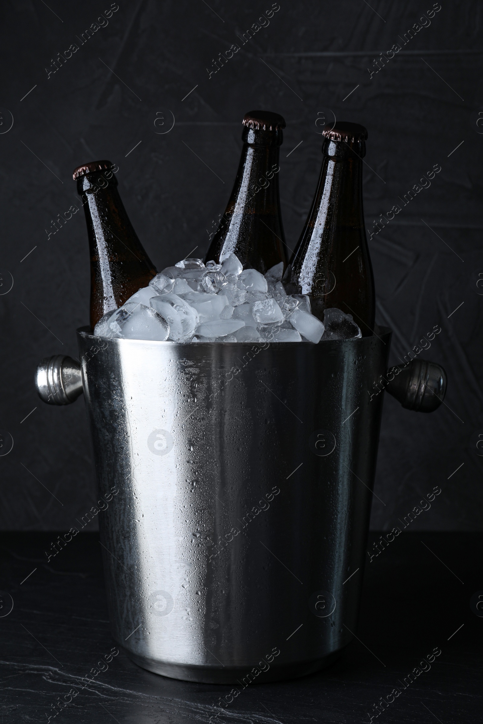 Photo of Metal bucket with beer and ice cubes on black table