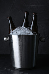 Metal bucket with beer and ice cubes on black table