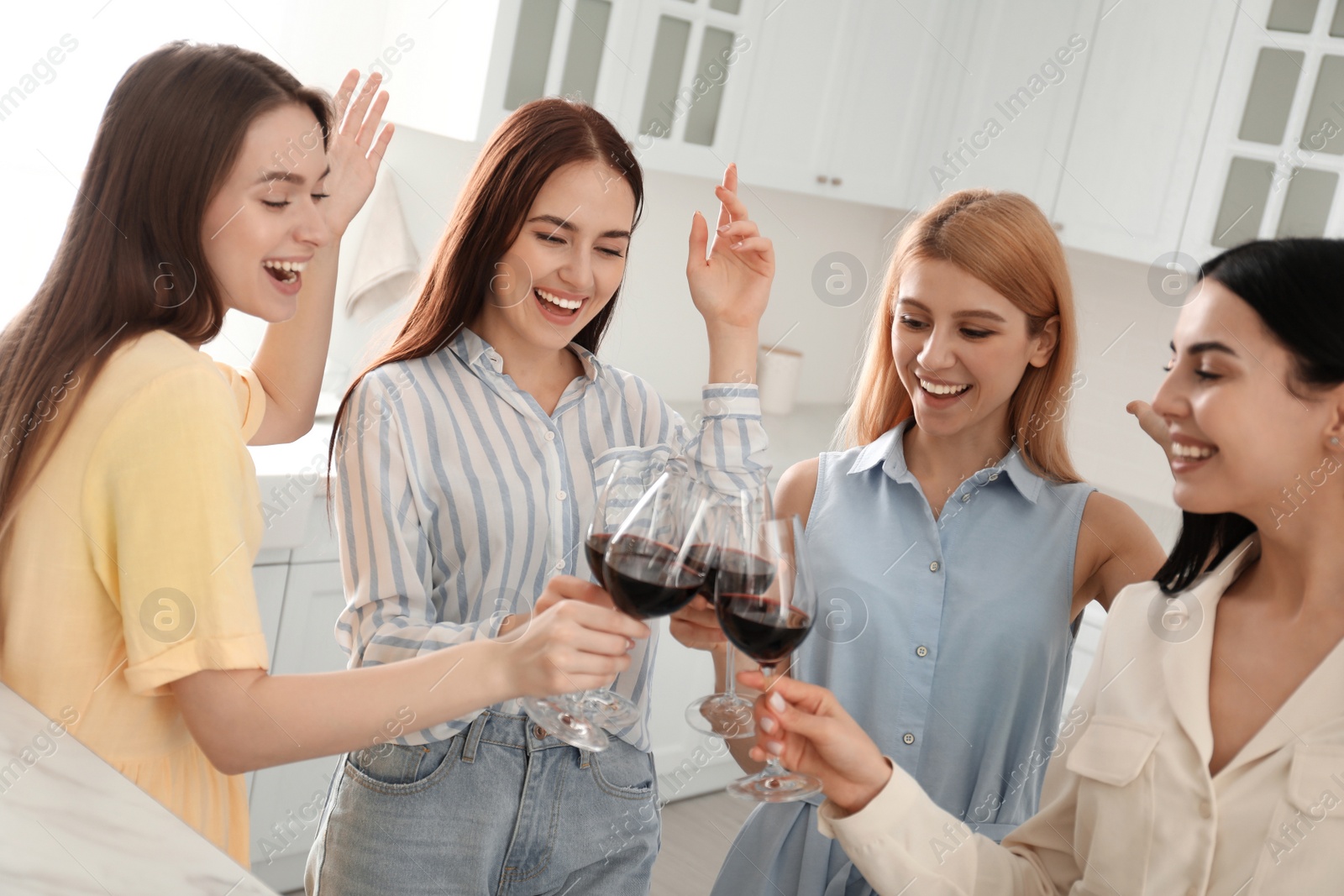 Photo of Beautiful young ladies clinking glasses of wine in kitchen. Women's Day