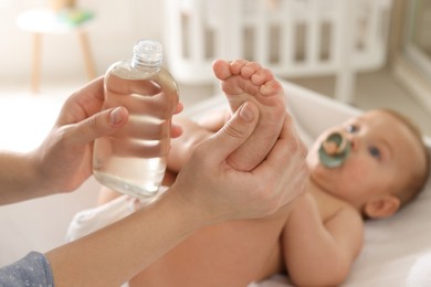 Photo of Mother massaging her baby with oil on changing table at home, closeup