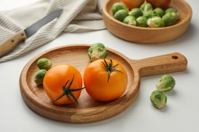 Photo of Cutting board with Brussels sprouts and tomatoes on white wooden table