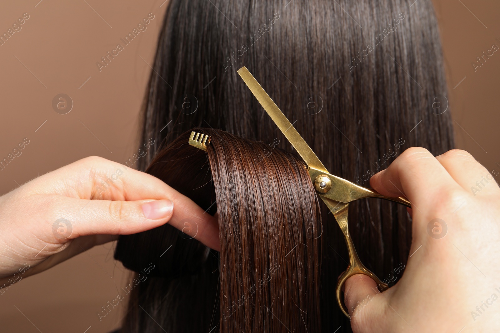 Photo of Hairdresser cutting client's hair with scissors on light brown background, closeup