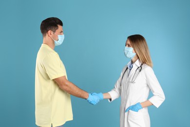 Photo of Doctor and patient in protective masks shaking hands on light blue background
