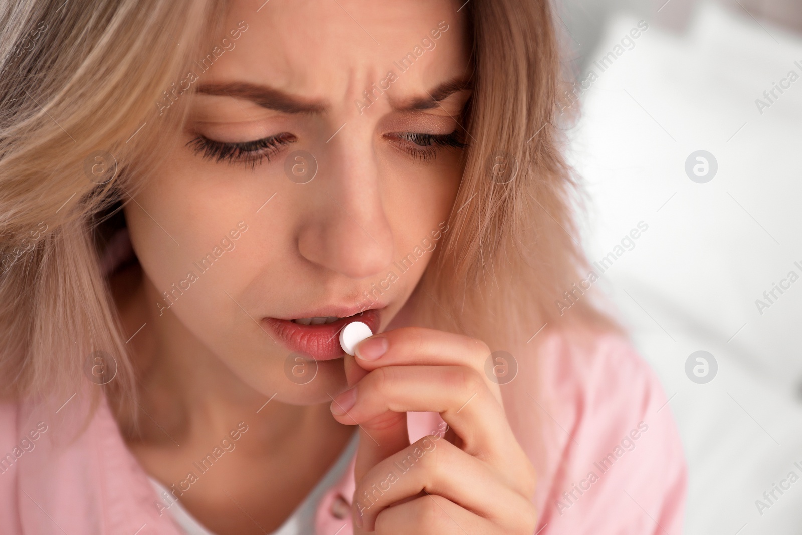 Photo of Upset young woman taking abortion pill on blurred background, closeup