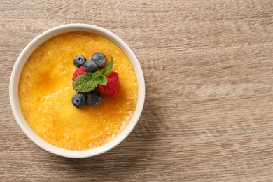 Photo of Delicious creme brulee with fresh berries on wooden table, top view. Space for text