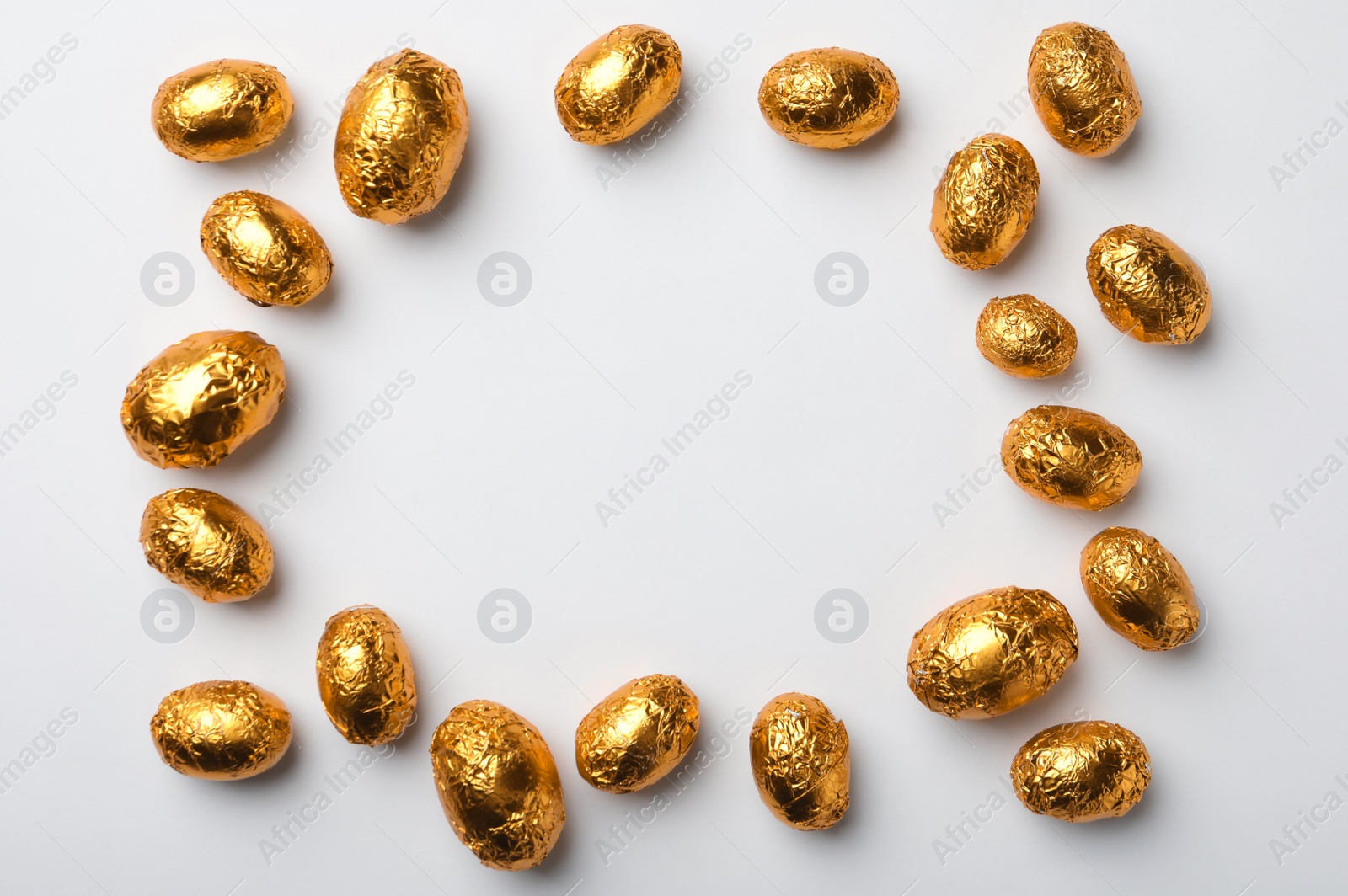 Photo of Frame of chocolate eggs wrapped in golden foil on white background, flat lay. Space for text