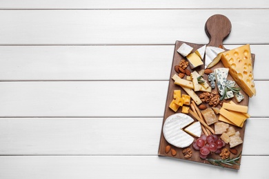 Photo of Cheese plate with grapes and nuts on white wooden table, top view. Space for text