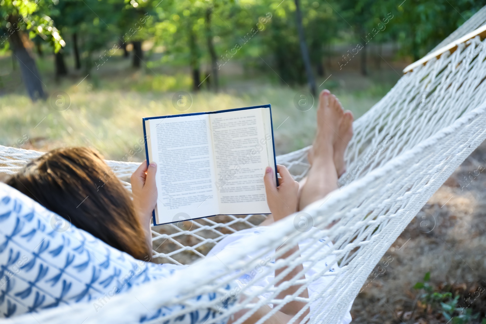 Photo of Young woman reading book in comfortable hammock at green garden