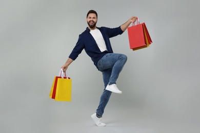 Happy man with many paper shopping bags dancing on grey background