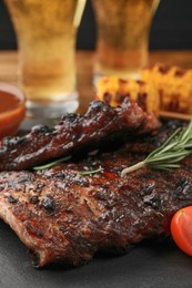 Glasses of beer, tasty fried ribs, grilled corn and sauce on wooden table, closeup