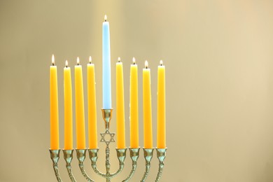 Photo of Hanukkah celebration. Menorah with burning candles on beige background, space for text