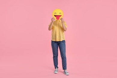 Photo of Woman covering face with emoticon sticking out tongue on pink background