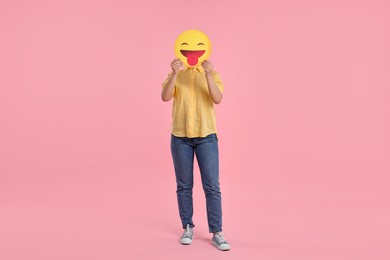 Woman covering face with emoticon sticking out tongue on pink background