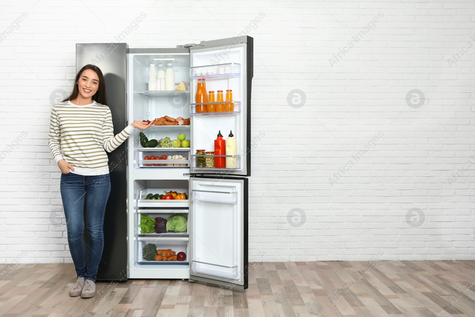 Photo of Happy young woman near open refrigerator indoors, space for text