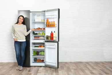 Photo of Happy young woman near open refrigerator indoors, space for text