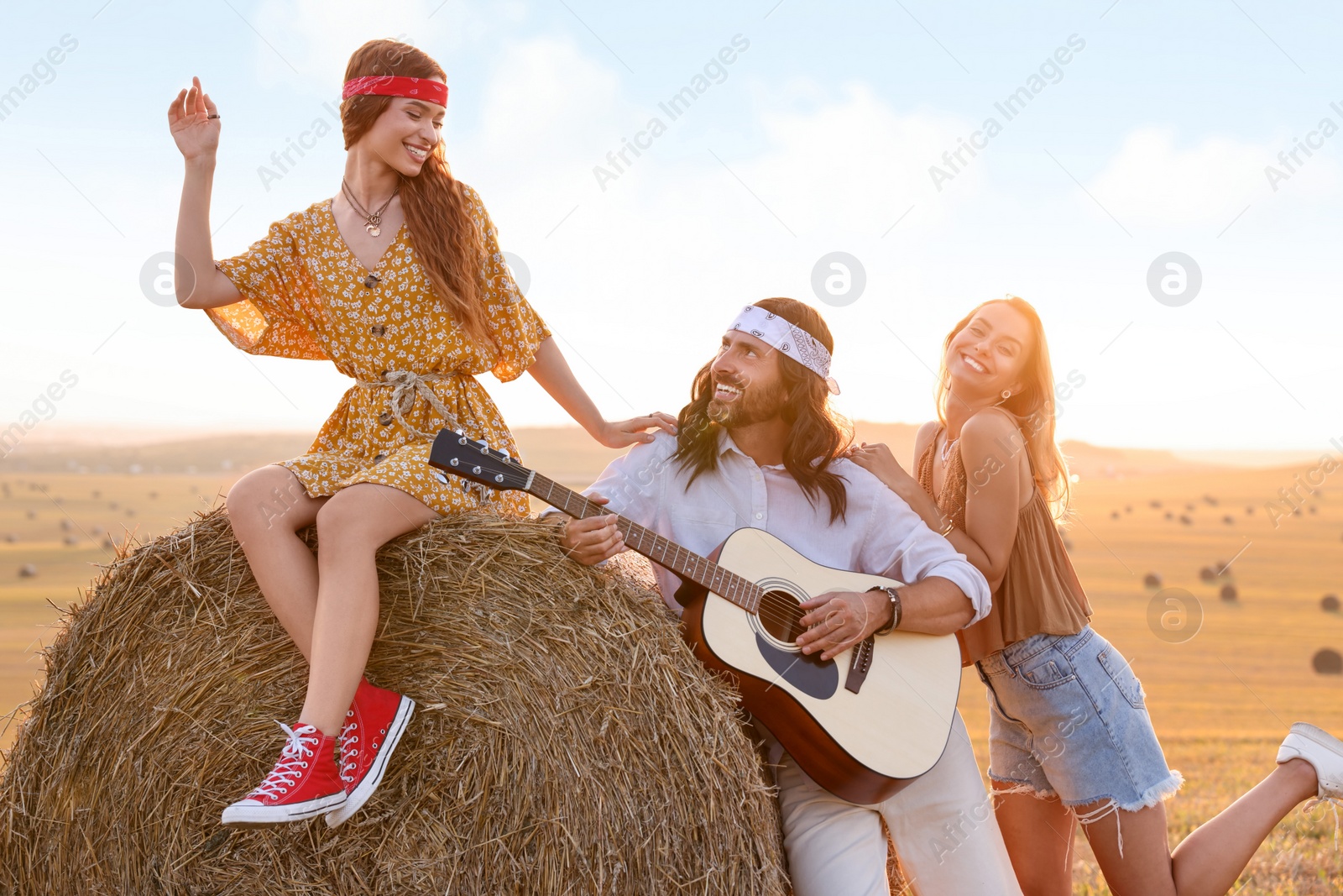 Photo of Beautiful hippie women listening to their friend playing guitar in field