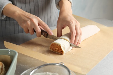 Woman cutting dough for cinnamon rolls on parchment at table, closeup