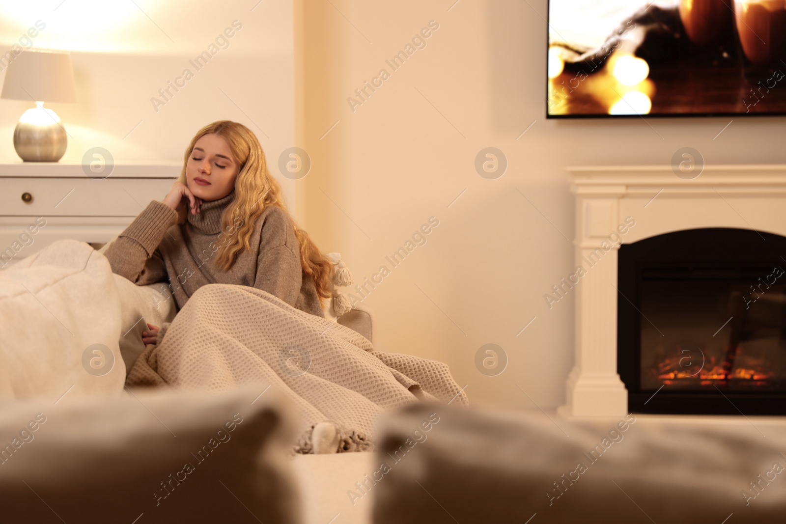 Photo of Beautiful young woman resting near fireplace at home