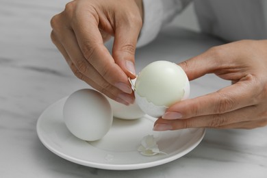 Photo of Woman peeling boiled egg at white marble table, closeup