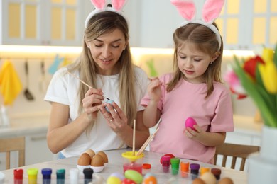 Photo of Easter celebration. Mother with her cute daughter painting eggs at white marble table in kitchen