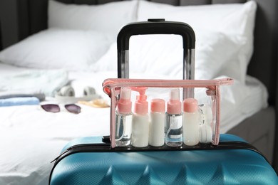 Photo of Cosmetic travel kit. Plastic bag with small containers of personal care products on suitcase in bedroom