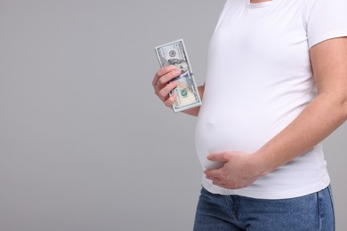 Surrogate mother. Pregnant woman with dollar banknotes on light grey background, closeup. Space for text