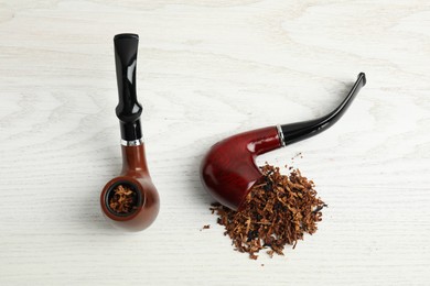 Photo of Smoking pipes with tobacco on white wooden table, flat lay
