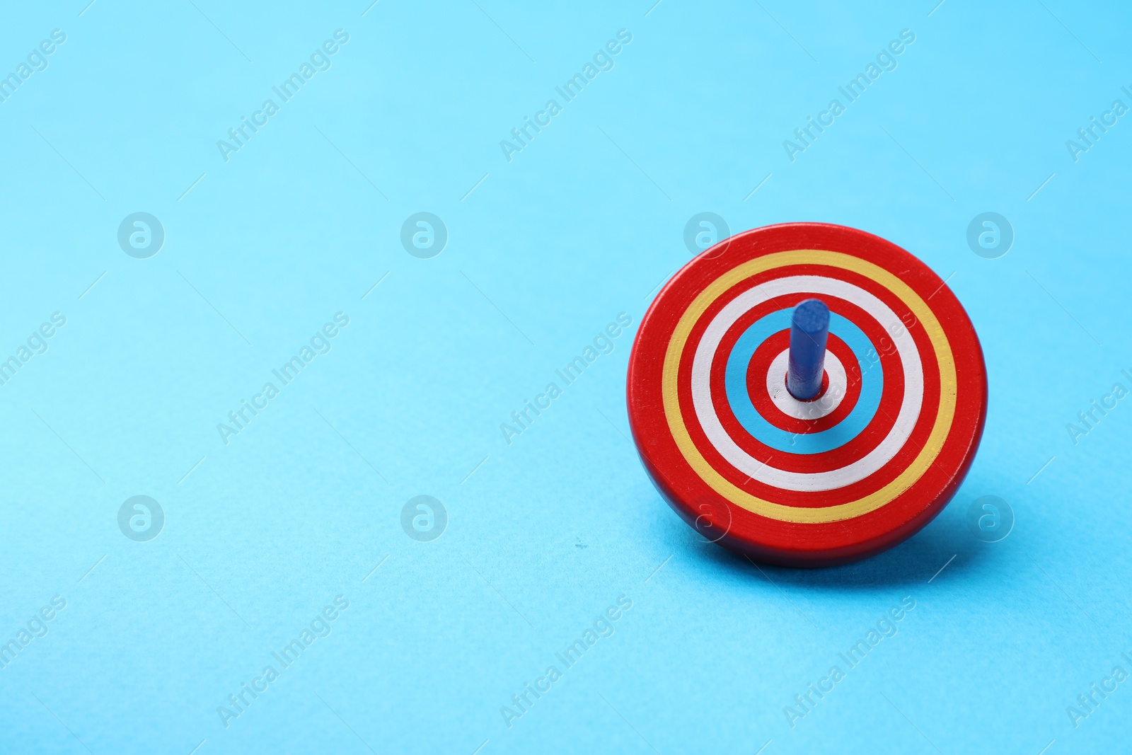 Photo of One colorful spinning top on light blue background, space for text