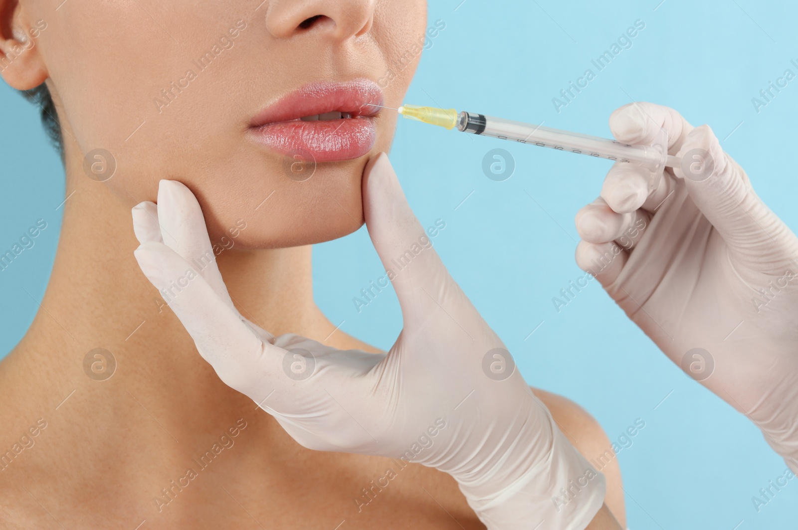 Photo of Woman getting lip injection on light blue background, closeup