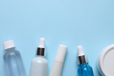 Photo of Many bottles and tube of cosmetic serum on light blue background, flat lay. Space for text